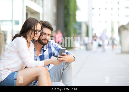 Couple using smart phone together while sitting on steps in city Stock Photo