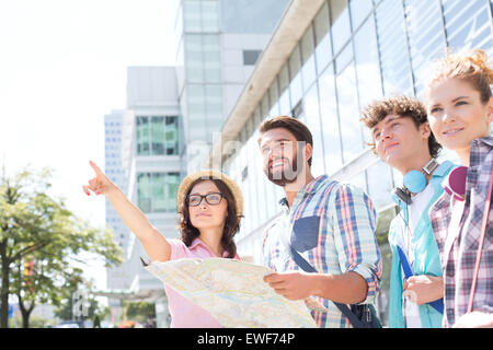 Happy friends with road map with woman pointing away in city Stock Photo