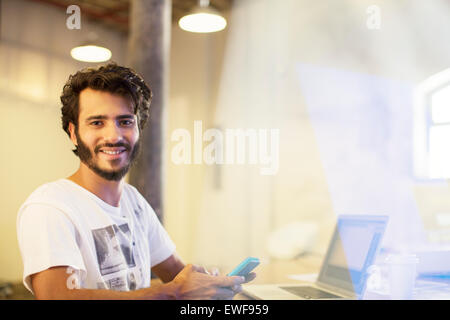 Portrait smiling casual businessman texting on cell phone at laptop Stock Photo