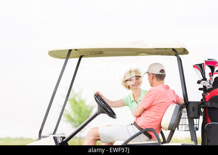 Happy woman looking at man while sitting in golf cart Stock Photo