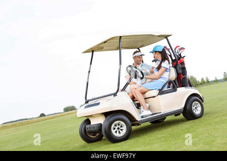 Couple looking at each other while sitting in golf cart against clear sky Stock Photo