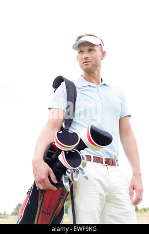 Low angle view of thoughtful mid-adult man carrying golf club bag against clear sky Stock Photo