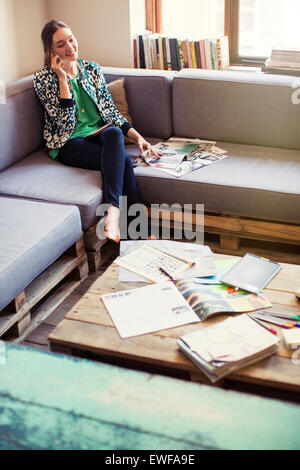 Creative businesswoman reviewing proofs and talking on cell phone on office sofa Stock Photo