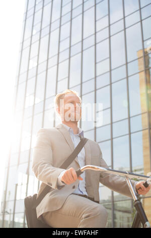 Low angle view of businessman riding bicycle outside office building on sunny day Stock Photo
