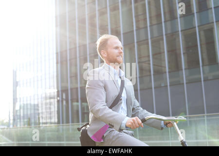 Businessman riding bicycle outside office building Stock Photo