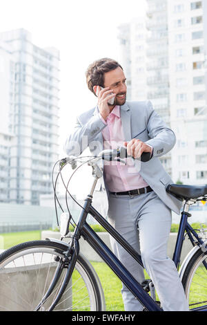 Businessman answering mobile phone while standing with bicycle outdoors Stock Photo