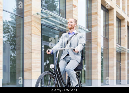 Smiling businessman riding bicycle outside building Stock Photo