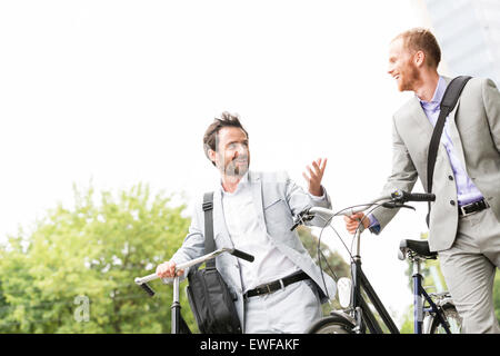 Businessmen talking while walking with bicycles outdoors Stock Photo