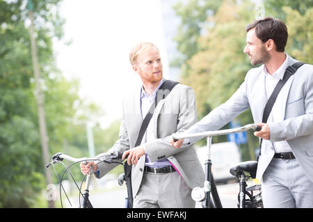 Businessmen looking at each other while holding bicycles outdoors Stock Photo