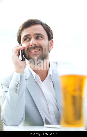 Happy businessman looking away while using mobile phone at outdoor restaurant Stock Photo