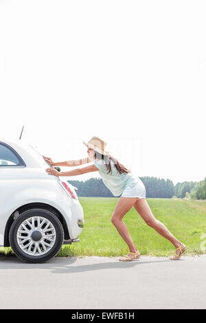 Full-length of woman pushing broken down car on country road Stock Photo