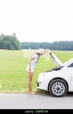 Side view of woman examining broken down car on country road Stock Photo