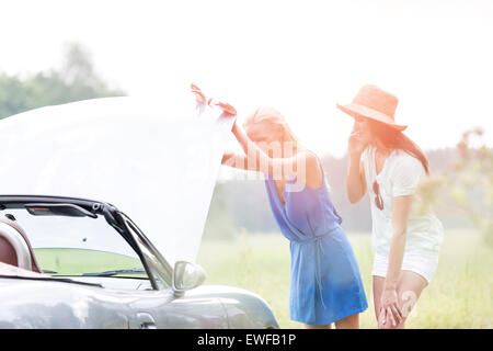 Friends examining broken down car on sunny day Stock Photo