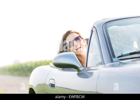 Excited woman enjoying road trip in convertible against clear sky Stock Photo