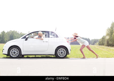 Woman pushing broken down car on country road Stock Photo