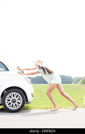 Side view of woman pushing broken down car on country road Stock Photo