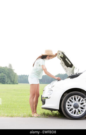 Side view of woman examining broken down car on country road Stock Photo