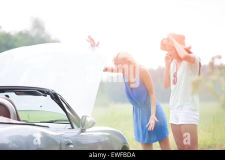 Worried female friends examining broken down car on sunny day Stock Photo