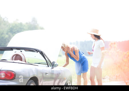 Female friends examining broken down car on country road Stock Photo