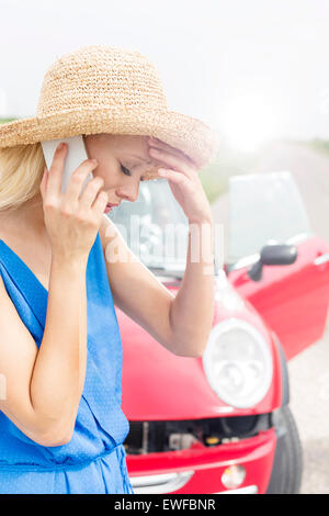 Tensed young woman using cell phone by broken down car Stock Photo