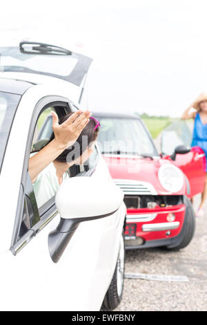 Angry woman gesturing while talking to female crashing car on road Stock Photo