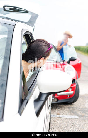 Woman looking at female crashing car on road Stock Photo