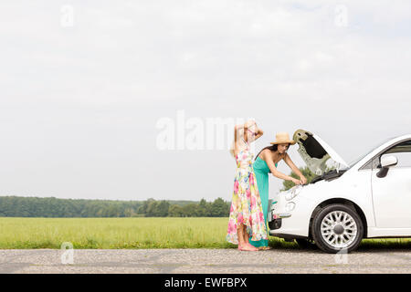 Friends examining broken down car on country road against clear sky Stock Photo