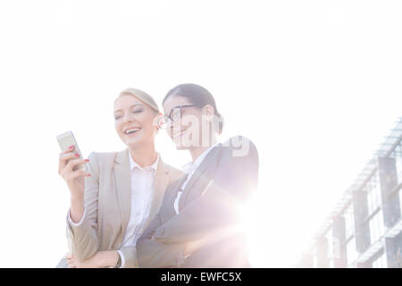 Low angle view of happy businesswomen using smart phone against clear sky on sunny day Stock Photo