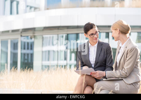 Businesswomen discussing over documents while sitting outside office building Stock Photo