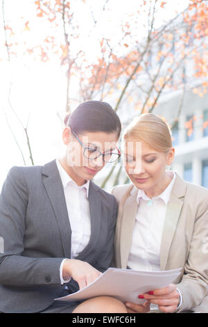 Businesswomen reading papers while sitting outdoors Stock Photo