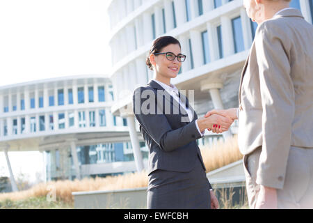 Happy businesswomen shaking hands outside office building Stock Photo