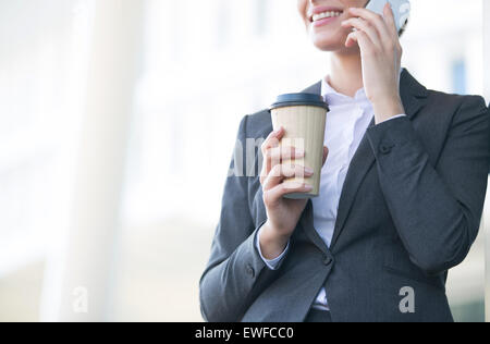 Midsection of businesswoman using cell phone while holding disposable cup outdoors Stock Photo