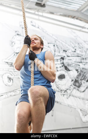 Low angle view of determined man climbing rope in crossfit gym Stock Photo