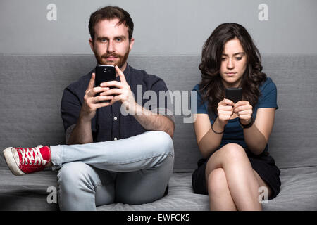 Young Silent Couple with Smartphones Sitting on a Couch Stock Photo
