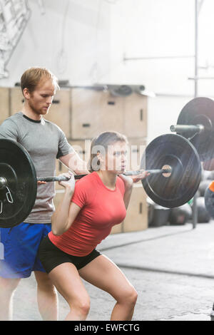 Man assisting woman in lifting barbell in crossfit gym Stock Photo