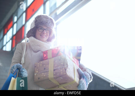 Smiling woman with stacked gifts and shopping standing by window during winter Stock Photo