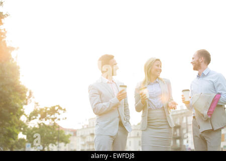 Happy businesspeople with disposable cups talking against clear sky on sunny day Stock Photo
