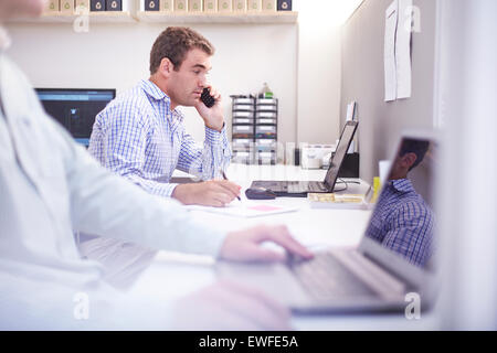 Architect talking on cell phone and working at laptop in office Stock Photo