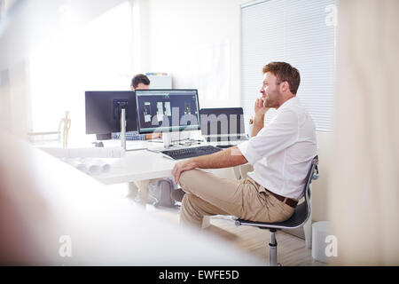 Architect talking on cell phone at computer in office Stock Photo