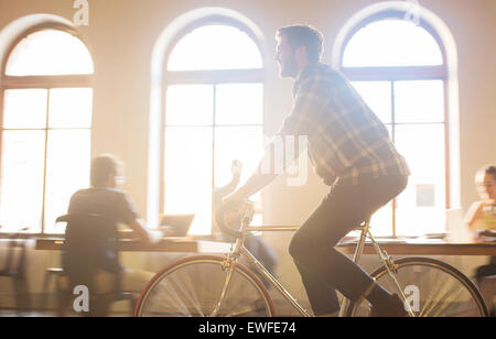 Casual businessman riding bicycle in sunny office Stock Photo