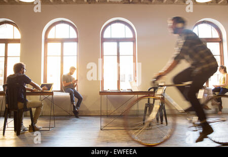 Casual businessman riding bicycle in open office Stock Photo