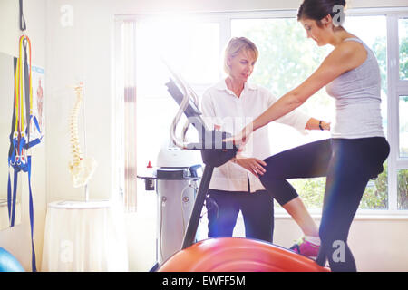 Physical therapist guiding woman on stationary bike Stock Photo