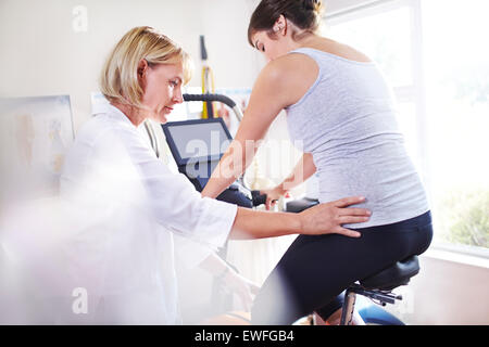 Physical therapist guiding woman’s hips on stationary bike Stock Photo