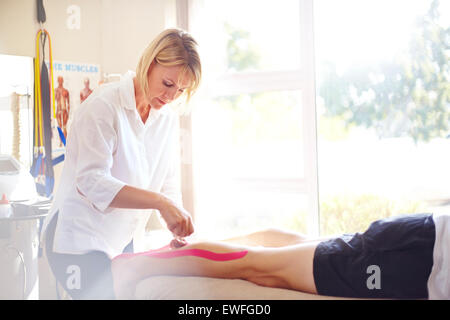 Physical therapist applying kinesiology tape to man’s leg Stock Photo