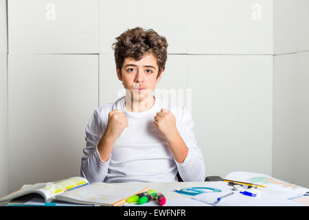 Caucasian young boy sits in front of homework: he is calm and confident and makes a gesture of success raising fists on industrial background Stock Photo