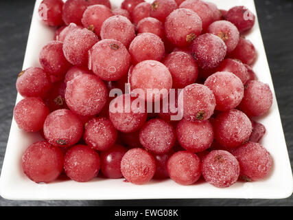 Top view of frozen currants covered with ice crystals in a white porcelain bowl on a slate platter Stock Photo