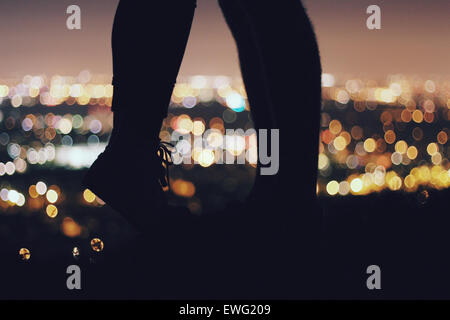 The silhouette of two pairs of legs is seen against the backdrop of city lights at night. The image captures the peaceful moment as the city skyline glows in the distance. Stock Photo