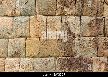 A close-up view of a stone brick wall composed of irregularly shaped blocks in varying shades of beige, gray, and brown. The surface shows signs of weathering, with patches of discoloration, lichen Stock Photo