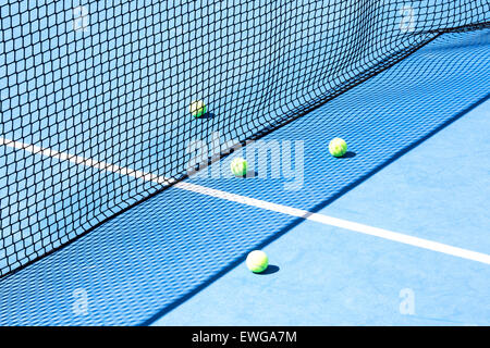Blue tennis court with network and four yellow balls on the floor Stock Photo