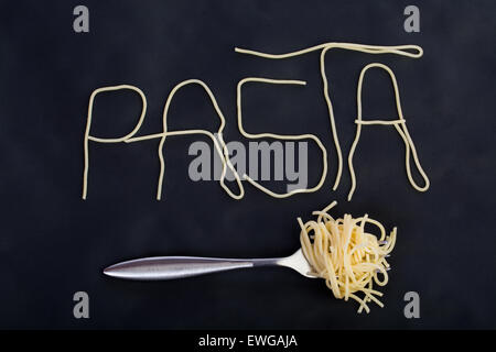 Word pasta made of cooked spaghetti with fork with rolled spagetti on it in black background Stock Photo